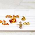 A collection of yellow and orange gemstone jewelry pieces, including a gold ring with a sunburst design arranged on a white display tray.