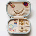 Open pale blue travel jewelry case displaying embroidered travel motifs and assorted gold-toned jewelry.