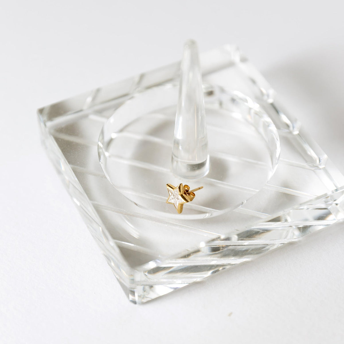 Gold five-point star stud earring with a pale faceted center displayed on clear glass.