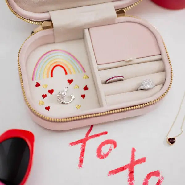 Pink travel jewelry box with embroidered rainbow and heart designs, containing rings and a necklace, on a white background.  Love in the Air Light Pink Velvet Embroidered Travel Jewelry Box. Jewelry Dallas.