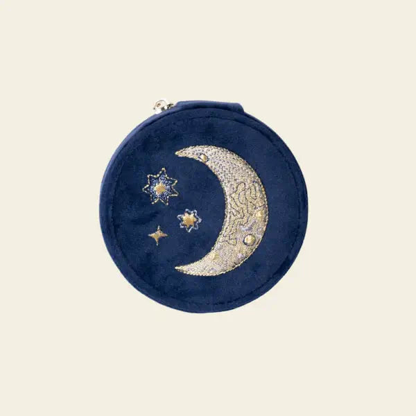 Round blue velvet mini travel jewelry box with embroidered moon and stars on a beige background. Mini Fly Me to the Moon Navy Blue Velvet Travel Jewelry Box. Jewelry Dallas.