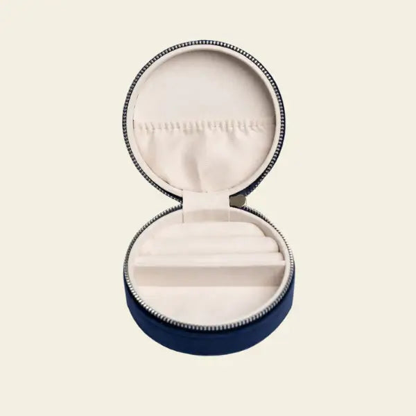 Round blue velvet mini travel jewelry box with embroidered moon and stars on a beige background. Mini Fly Me to the Moon Navy Blue Velvet Travel Jewelry Box. Jewelry Dallas.