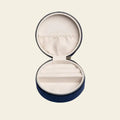 Round blue velvet mini travel jewelry box with embroidered moon and stars on a beige background. Mini Fly Me to the Moon Navy Blue Velvet Travel Jewelry Box. Jewelry Dallas.