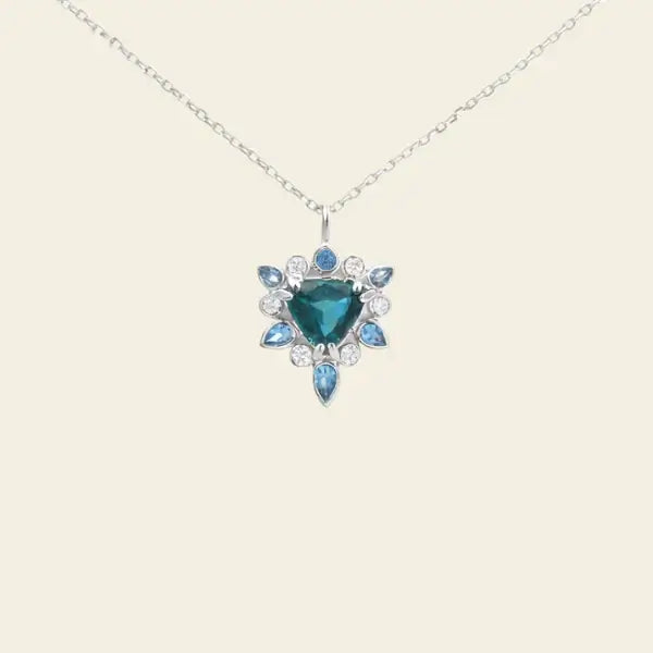 Necklace with a blue gemstone pendant on a beige background. One-of-a-Kind Pendant with Teal Blue Sapphire. Captivating teal blue sapphire set in 14K white gold. The pendant hangs from a delicate yet durable 1.3mm 14K white gold cable chain. Jewelry Dallas.