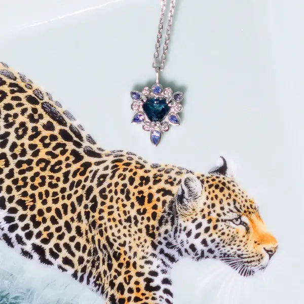 Leopard with a necklace featuring a blue gemstone on a light blue background. One-of-a-Kind Pendant with Teal Blue Sapphire. Captivating teal blue sapphire set in 14K white gold. The pendant hangs from a delicate yet durable 1.3mm 14K white gold cable chain. Jewelry Dallas.