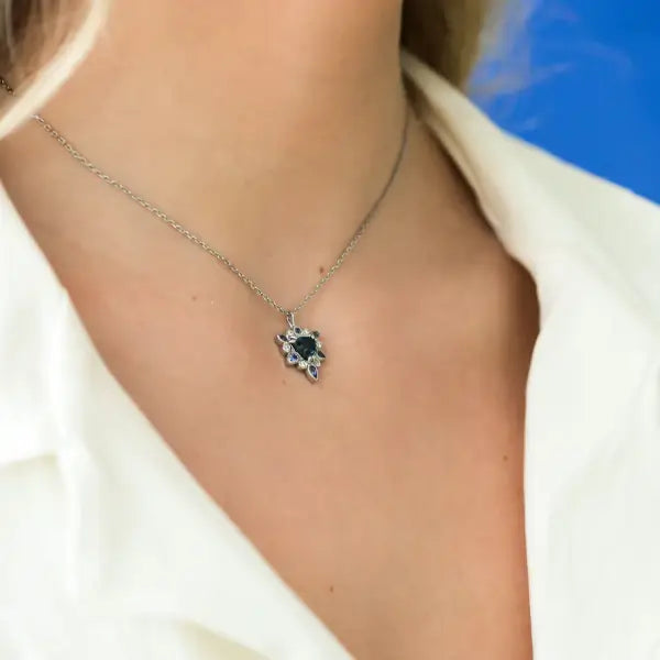 Necklace with a pendant worn by a person against a blue background. One-of-a-Kind Pendant with Teal Blue Sapphire. Captivating teal blue sapphire set in 14K white gold. The pendant hangs from a delicate yet durable 1.3mm 14K white gold cable chain. Jewelry Dallas.