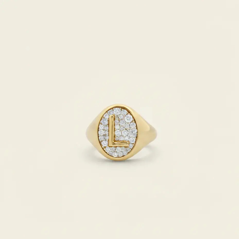 Gold oval pinky ring with 'L' and diamond pave accents on a beige background. Oval Pinky Ring. Solid gold and natural diamonds. Jewelry Dallas.