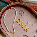 Jewelry set including a pearl necklace, gold 'CMR' letters, and butterfly pendant on a pink velvet jewelry tray. Pink Velvet Jewelry Tray. Jewelry Dallas.