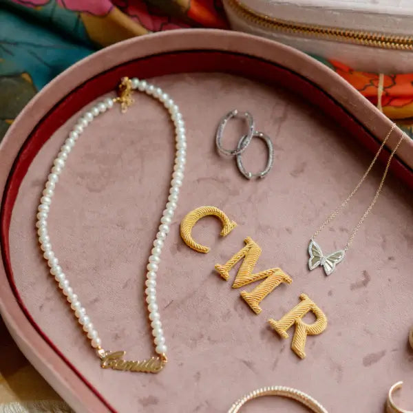 Jewelry set including a pearl necklace, gold 'CMR' letters, and butterfly pendant on a pink velvet jewelry tray. Pink Velvet Jewelry Tray. Jewelry Dallas.