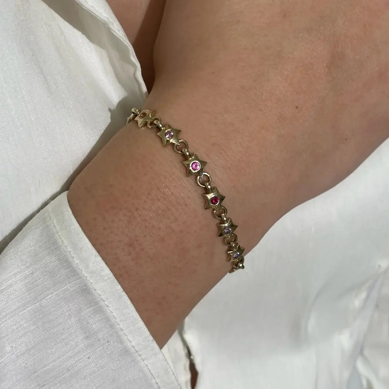 Gold bracelet with star-shaped charms and rainbow gemstones on a wrist. Rainbow Star Bracelet. Crafted in solid 14K yellow gold, each petite star is set with vibrant 0.80 carats of colored sapphires. Jewelry Dallas.