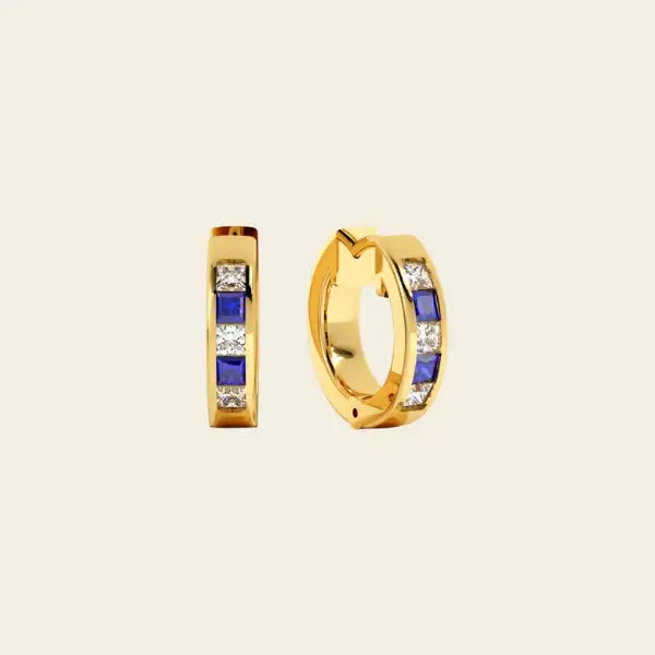 Gold huggie earrings with blue sapphires and diamonds on a beige background. Sapphire Checkered Huggies. Solid gold with natural sapphires and diamonds. Jewelry Dallas.