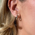 Close-up of a person wearing gold huggie earrings with blue sapphires and diamonds. Sapphire Checkered Huggies. Solid gold with natural sapphires and diamonds. Jewelry Dallas.
