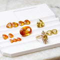 A collection of yellow gemstone jewelry pieces, including a gold ring with a sunburst halo and matching stud earrings, arranged on a white display tray over a light marble surface.

