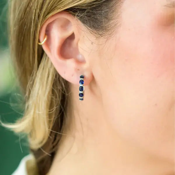 Close-up of an ear wearing hoop earrings with blue sapphires and diamonds. Sapphire and Pave Diamond Hoops. Material: Solid 18kt White Gold with 0.47 carats of Natural Diamonds and Sapphires totaling 2.23 carats. Jewelry Dallas.