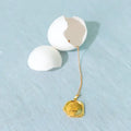 Gold necklace with a pendant inside a cracked white egg on a light blue background. Wax Seal Pendant Length: 16