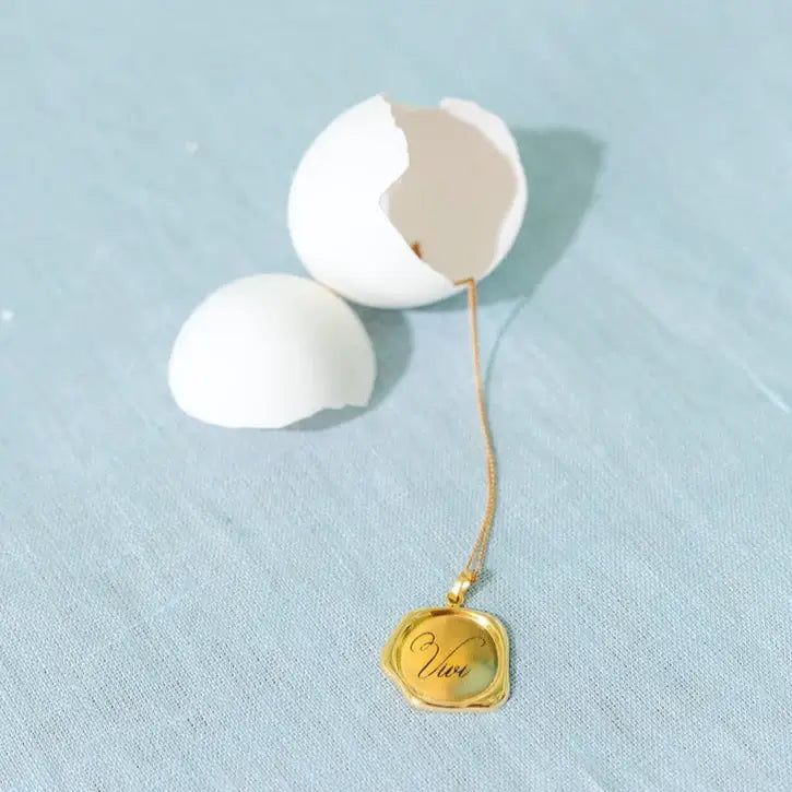 Gold necklace with a pendant inside a cracked white egg on a light blue background. Wax Seal Pendant Length: 16"+2" Link Chain
Material: 14kt Gold Over Sterling Silver .925 or solid 14kt Gold. Jewelry Dallas.